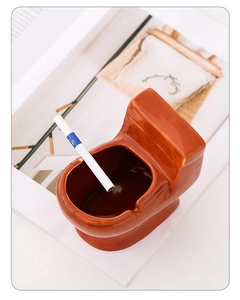 Detail shot of a brown toilet-shaped ceramic ashtray on a desk with magazines