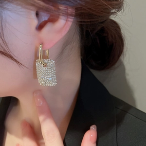 Détail de boucles d'oreilles dorées rectangulaires serties de cristaux sur un mannequin
