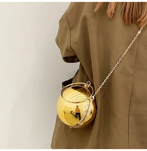 Dettaglio di una borsa a sfera dorata con catena in metallo indossata da una modella