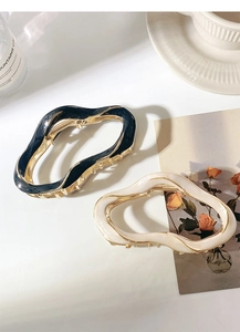 Detail of irregular wave metal hair claws in black and cream with golden base