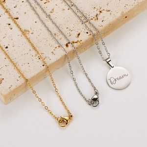 Polished stainless steel necklaces with engraved Dream pendant on a stone background