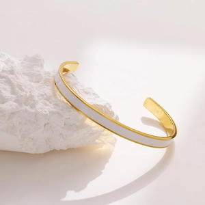 Detailansicht eines goldenen Edelstahl-Armreifs mit weißem Emaille-Inlay auf einem Stein