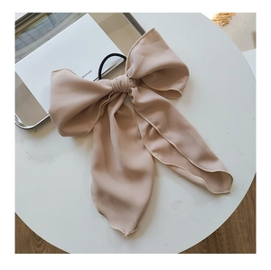 Detail of a large apricot chiffon bow hair tie with elastic band on a white table