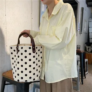 Close-up of retro polka dot canvas bag with brown leather handles and metal rivets