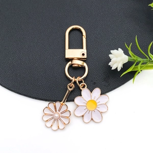 Detailed macro of golden daisy flower keychain charms with white enamel and pearl accents
