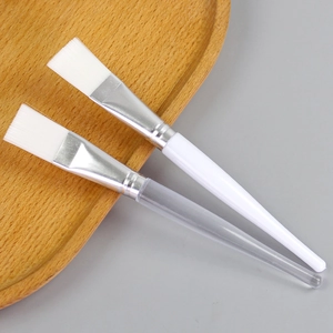 DIY facial mask brushes with crystal clear and white handles on a wooden tray