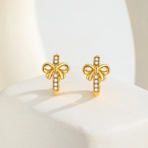 Golden cross and bow drop earrings with clear zircons on a white stone pedestal