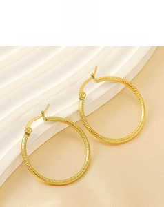 Detail shot of golden hoop earrings with grooved texture on champagne satin background