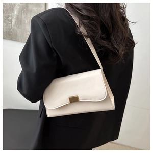 Detail of a minimalist cream crossbody bag with gold buckle styled on a black blazer