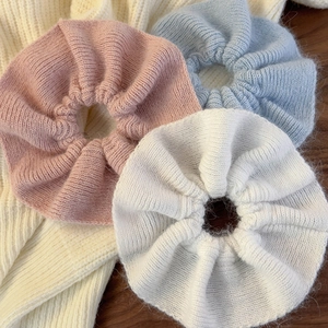 Close-up of pink, blue, and white ruffled knit hair scrunchies on a soft wooden surface