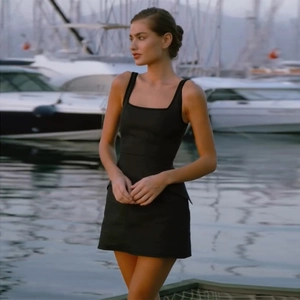 Dettaglio dell'elegante mini abito nero con scollo quadrato indossato in un porto turistico