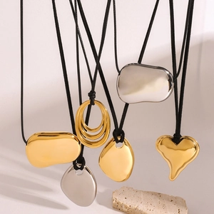 Irregular polished gold and silver pendant necklaces on black cord over stone background