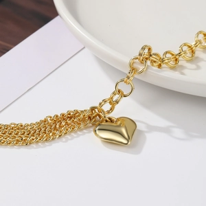 Detailed close-up of a layered gold chain bracelet featuring a polished heart pendant