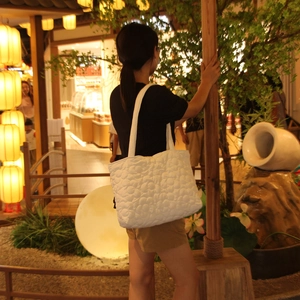 Detailed view of a white quilted tote bag with floral 3D texture on a shoulder strap
