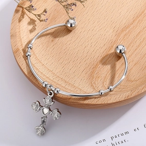 Detail of silver vintage open bangle with rose cross heart pendant on wooden tray
