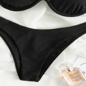 Flat lay of black ribbed bikini set with underwire cups on white fabric background