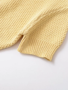 Detail of waffle knit texture and side split hem on a cream yellow cardigan jacket