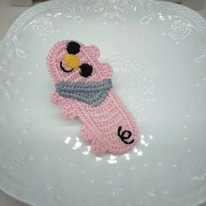 Dettaglio di un fermaglio per capelli in maglia rosa a forma di maialino con sciarpa
