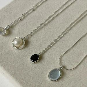 Detail of four silver necklaces with pearl, black gem, moonstone, and grey stone pendants