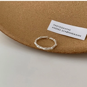 Close-up of minimalist silver open ring with twisted rope texture on a cork tray