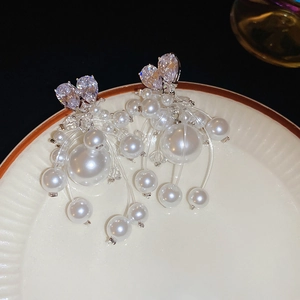 Dettaglio di orecchini a cuore in zircone con lunghe nappe di perle su vassoio ceramico