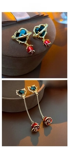 Detail of gold thorn heart earrings with red enamel roses on a dark velvet display