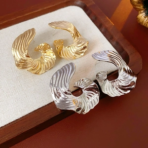 Detail of twisted textured earrings in gold and silver finish on a wooden tray