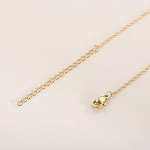 Close-up of golden necklace lobster clasp and adjustable extension chain on beige surface