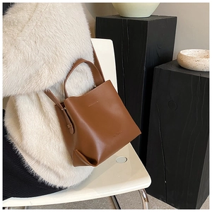 Detailed side view of a brown vintage leather bucket bag carried by a model in a cozy coat