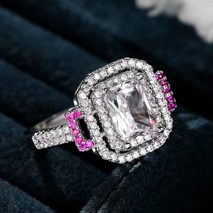 Macro view of princess cut clear gemstone ring with pink side stones on blue velvet
