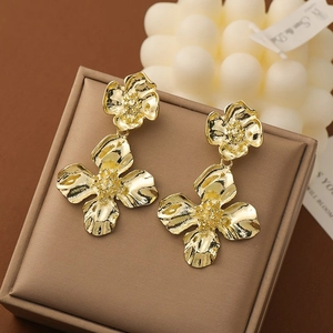 Elegant gold metal flower drop earrings displayed on a textured jewelry box with candles