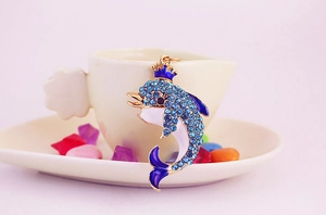 Close-up of golden dolphin keychain with blue rhinestones and a crown on white dish