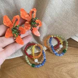 Detailed view of handmade beaded flower stud earrings and colorful bead rings on burlap