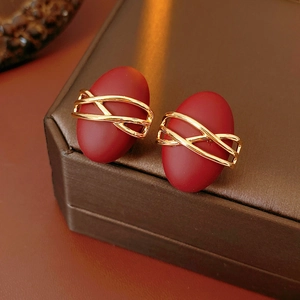 Close-up of red matte oval earrings with gold intertwined metal on a brown textured box