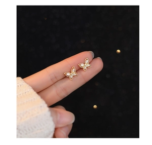 Close-up of golden butterfly stud earrings with sparkling cubic zirconia on fingertips