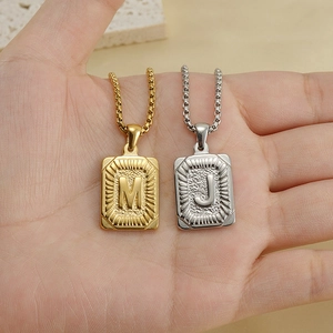 Detail of square gold and silver 18K stainless steel pendants with M and J letter engravings