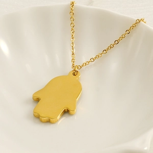 Golden Hamsa Hand pendant necklace in stainless steel on white ceramic display plate