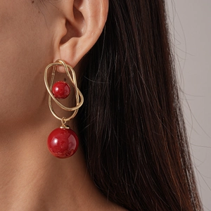 Close-up of geometric gold hoop earring with red sphere accents on a model ear