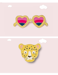 Detail of heart sunglasses and leopard head enamel pins on soft pink background