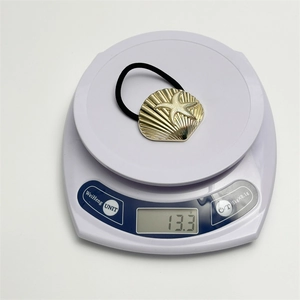 Macro shot of a black hair tie with gold shell charms on a digital scale weighing 13.3g