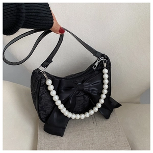 Detail of black pleated fabric handbag with oversized satin bow and pearl chain handle