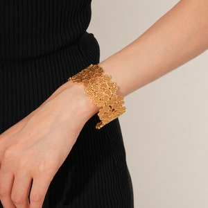 Close-up of wide gold hollow clover flower cuff bracelet on a model wrist