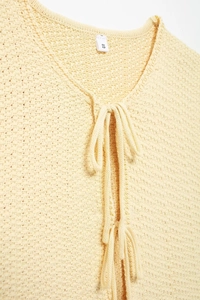 Macro detail of beige knit vest showing the mesh texture, bow tie-up and size S label