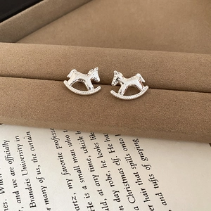 Macro shot of silver rocking horse stud earrings on brown velvet and vintage book