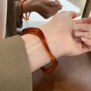 Close-up of amber resin bracelet with irregular wave design worn on woman's wrist
