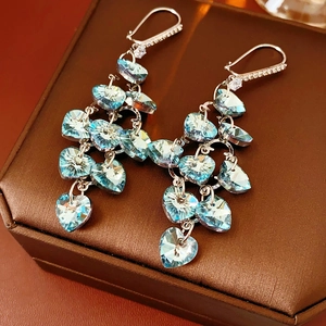 Detail of silver heart-shaped fringe earrings with blue faceted crystal on a jewelry box