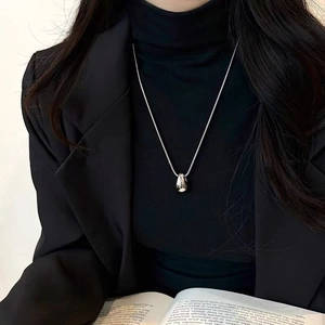 Minimalist silver teardrop pendant necklace with a fine chain worn over a dark outfit