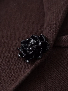 Gros plan d'un bouton décoratif fleur 3D noire sur un blazer en maille marron foncé