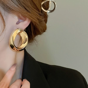 Detail of twisted geometric gold hoop earrings with metallic luster on model