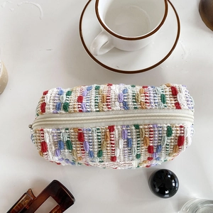 Colorful woven makeup bag with zipper and All The Little Things label on white desk